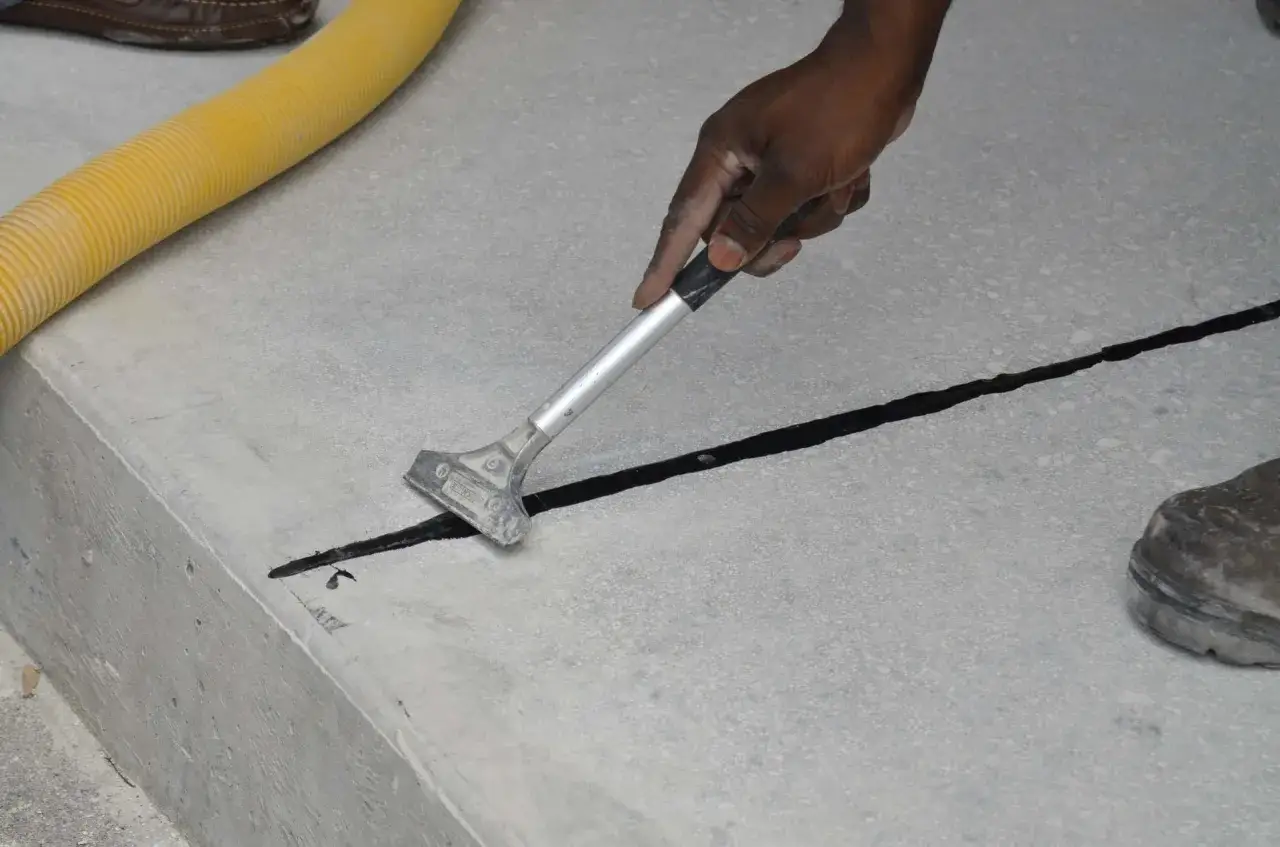 Maintenant, on peut couler une dalle en plusieurs fois. Un ouvrier applique un produit noir dans une jointure de b&eacute;ton avec un grattoir.