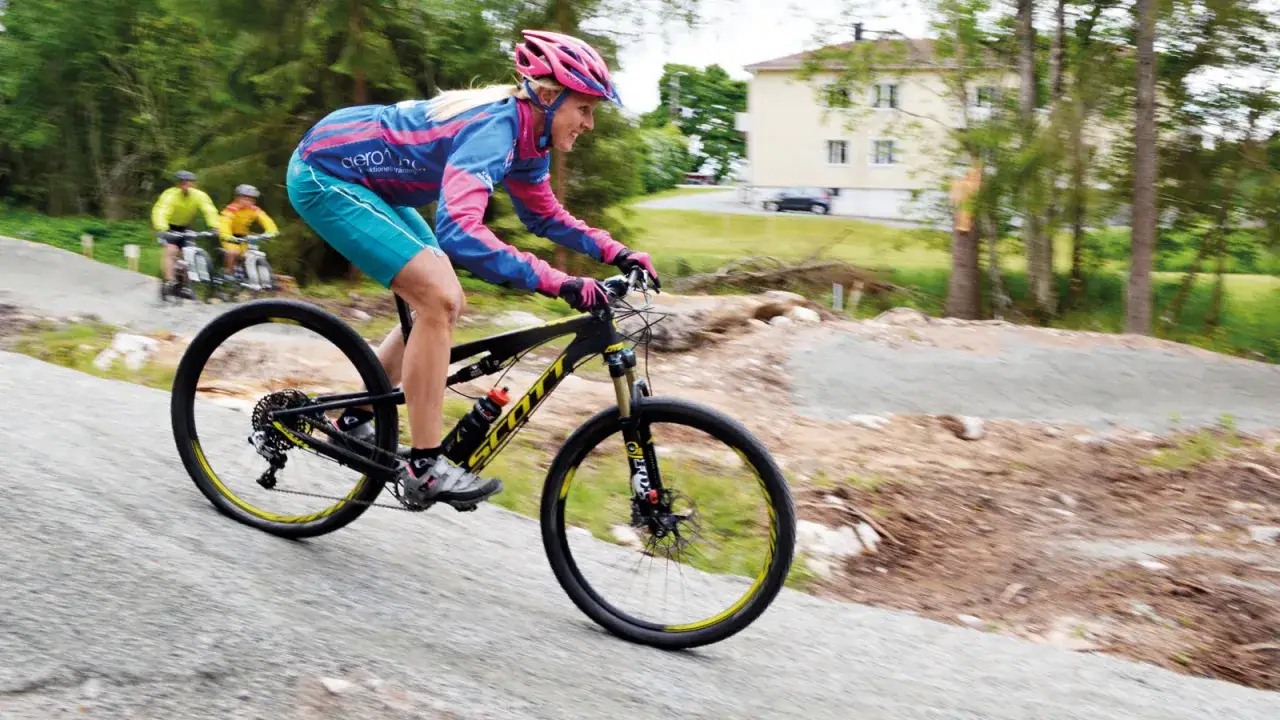 Kvinna cyklar på mtb leder i Sverige. Två män cyklar i bakgrunden.