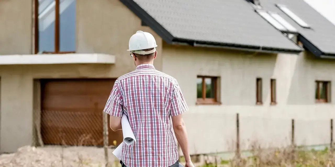 Un architecte en casque blanc, portant des plans, examine une maison en construction. Avis Camif Habitat : un projet immobilier en cours.