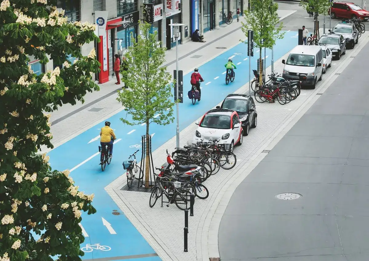 Fahrradfahrer auf blauem Radweg, Autos und B&auml;ume symbolisieren nachhaltige Quartiersentwicklung in einer modernen Stadt.