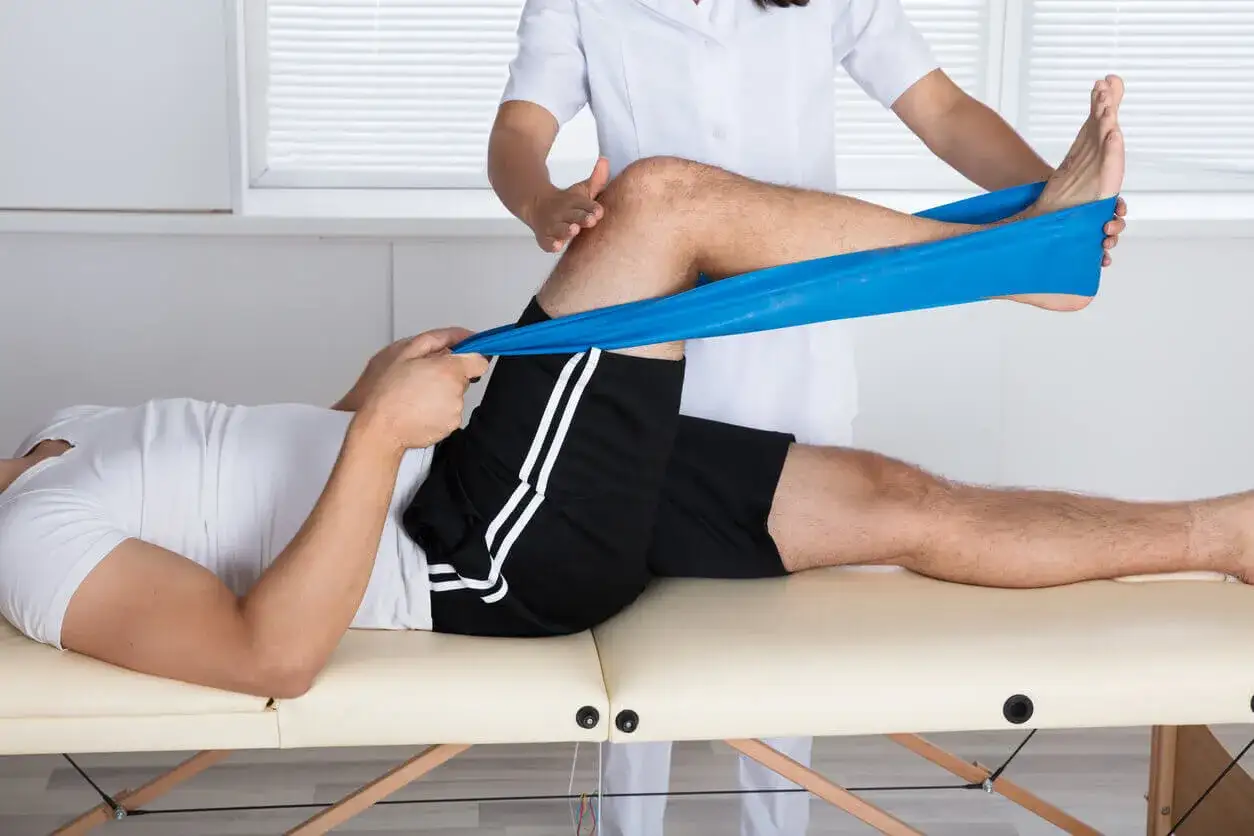 Physiotherapeut dehnt Bein eines Mannes mit blauem Theraband, um Plica-Syndrom nach Liebscher & Bracht zu behandeln.