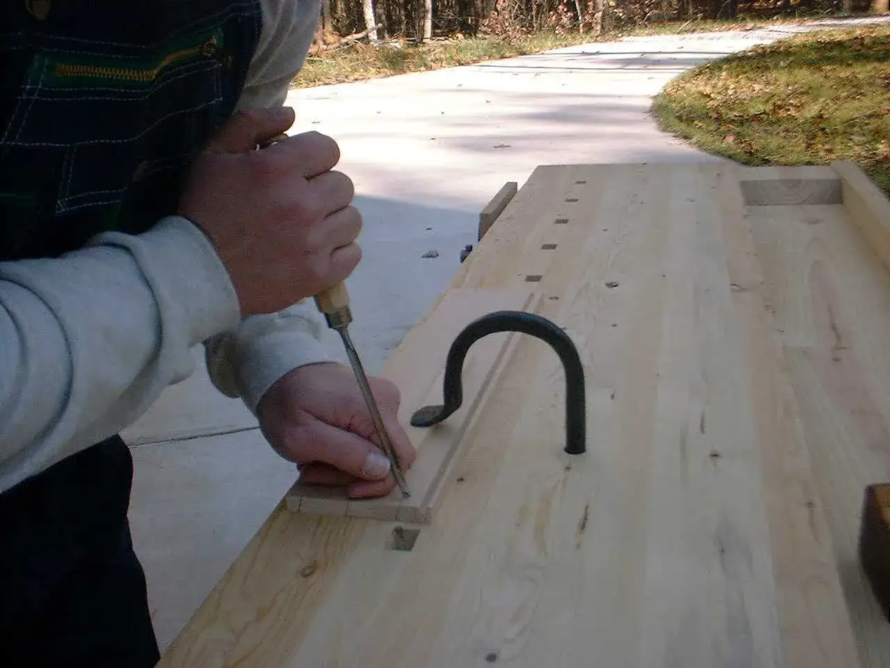 Un menuisier utilise un ciseau pour travailler sur un plan établi en bois.