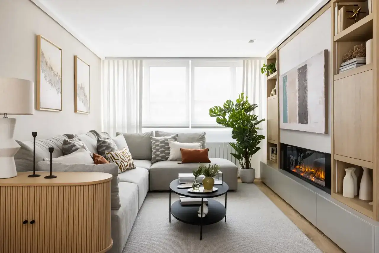 Sof&aacute; modular gris, mesa de centro redonda, chimenea moderna y estanter&iacute;as de madera. Las medidas del sal&oacute;n son ideales para este dise&ntilde;o acogedor.