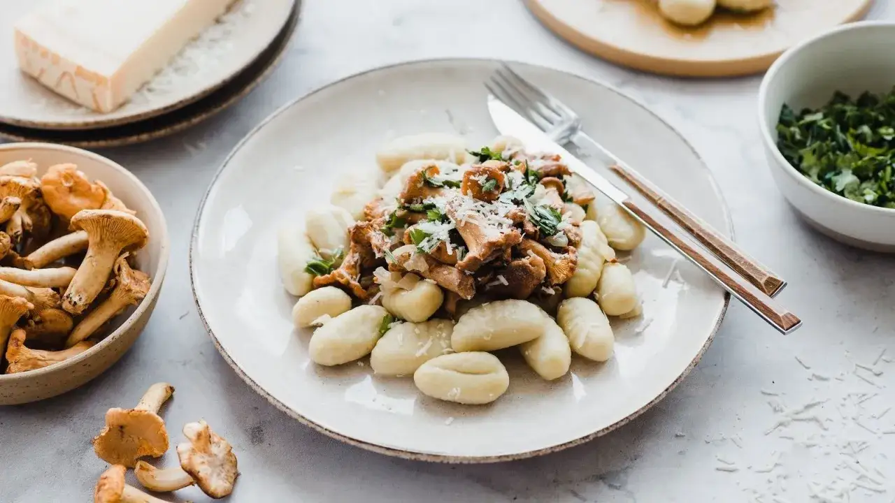 Pyszne gnocchi z kurkami, posypane parmezanem i świeżą natką pietruszki. Obok miseczka z kurkami i kawałek sera.