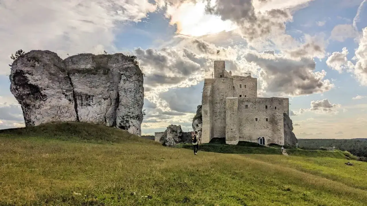 Zamek Mirów majestatycznie wznosi się na skale, otoczony zielonymi wzgórzami i dramatycznym, chmurnym niebem.