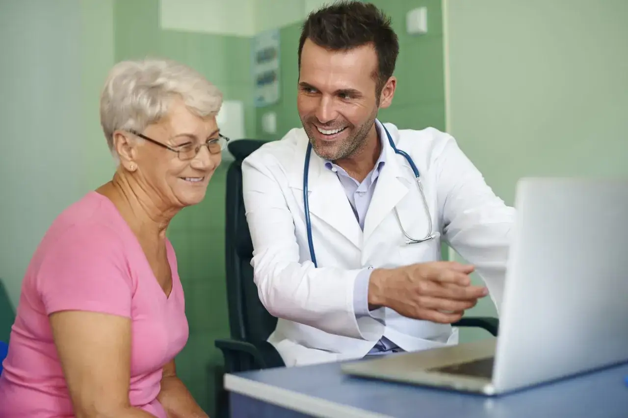 Médecin souriant expliquant un test mémoire personne agée sur un ordinateur portable.