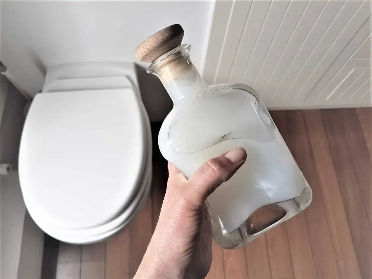 Main tenant une bouteille en verre remplie d'un produit wc maison, pr&ecirc;t &agrave; l'emploi.