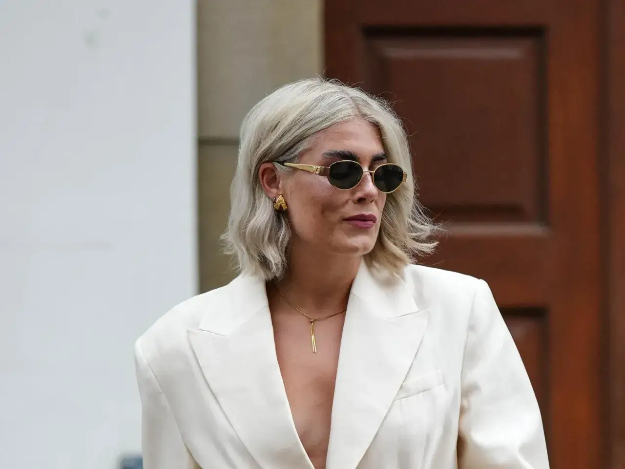 Stilvolle Frau mit shaggy bob ab 50, tr&auml;gt wei&szlig;en Blazer, Sonnenbrille und auff&auml;lligen Schmuck.