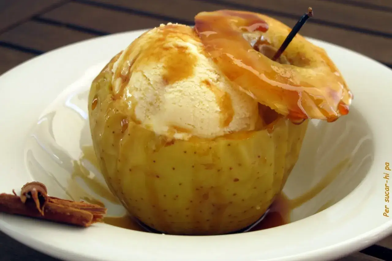 Delicioso helado de manzana servido en una manzana horneada, bañado en caramelo y acompañado de canela.