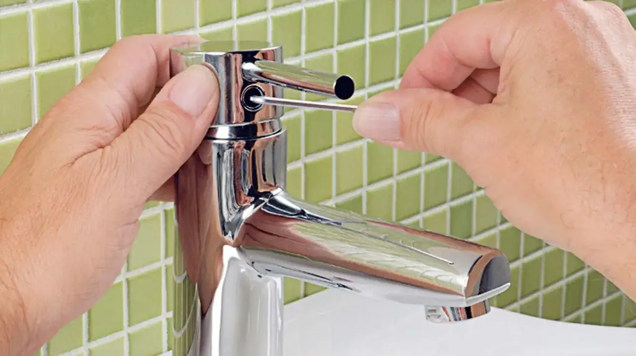 Hände reparieren einen tropfenden Wasserhahn mit einem kleinen Werkzeug.