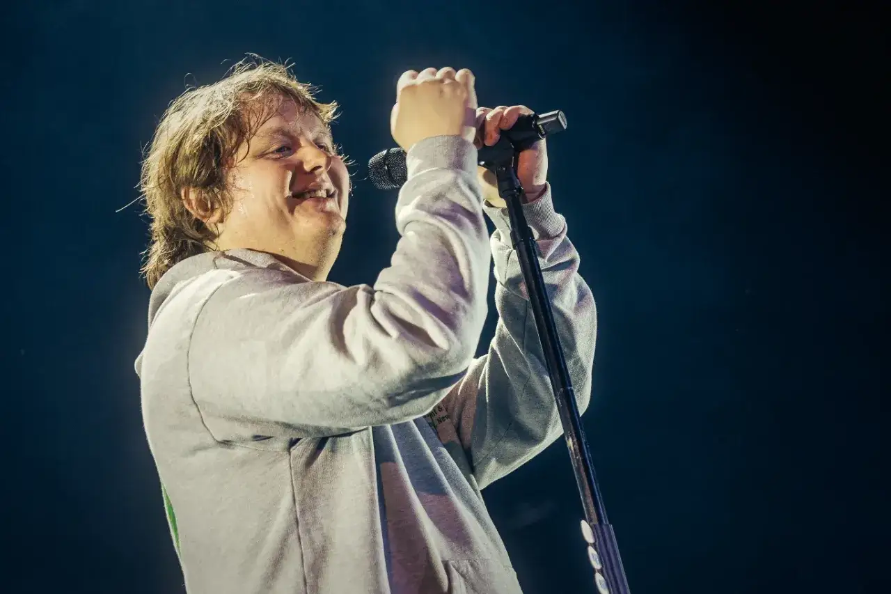 Lewis Capaldi, mimo choroby Tourette'a, śpiewa z pasją na koncercie, trzymając mikrofon.