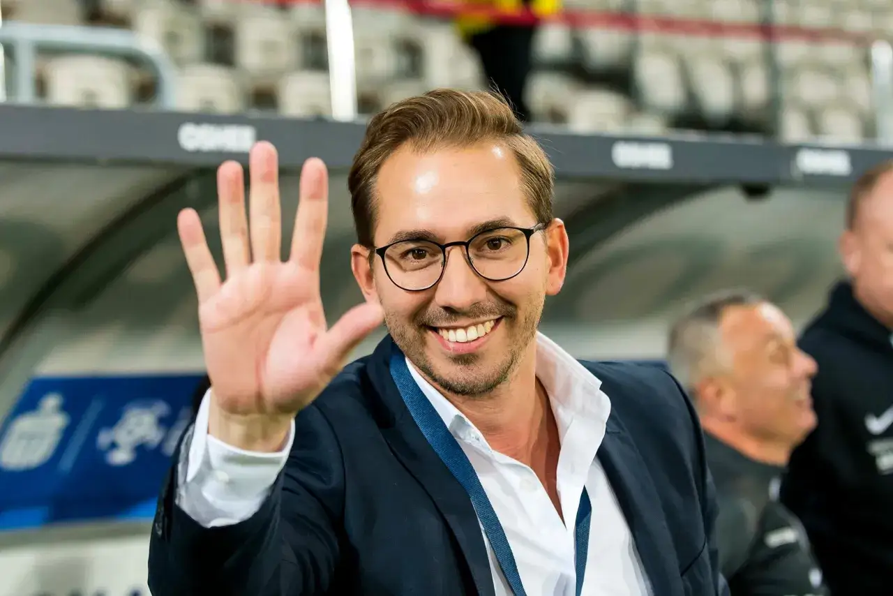 Uśmiechnięty dyrektor sportowy w okularach macha do fanów.