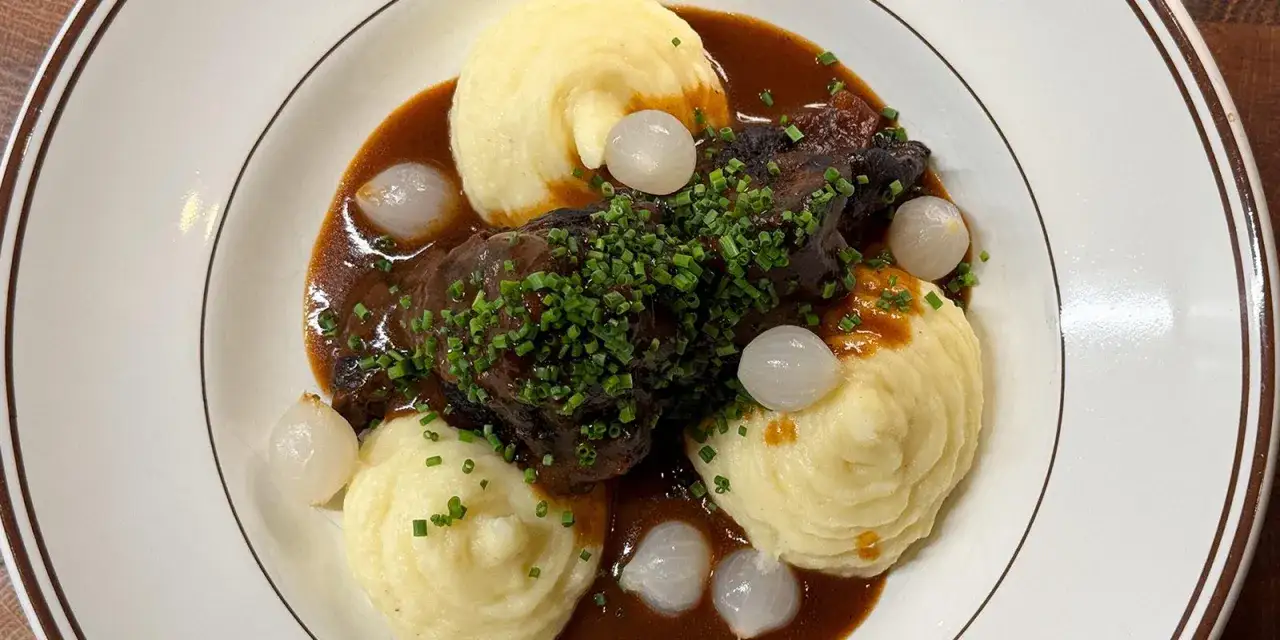 En mustig gryta med vin till oxkind, serverad med krämigt potatismos, små lökar och toppad med färsk gräslök.