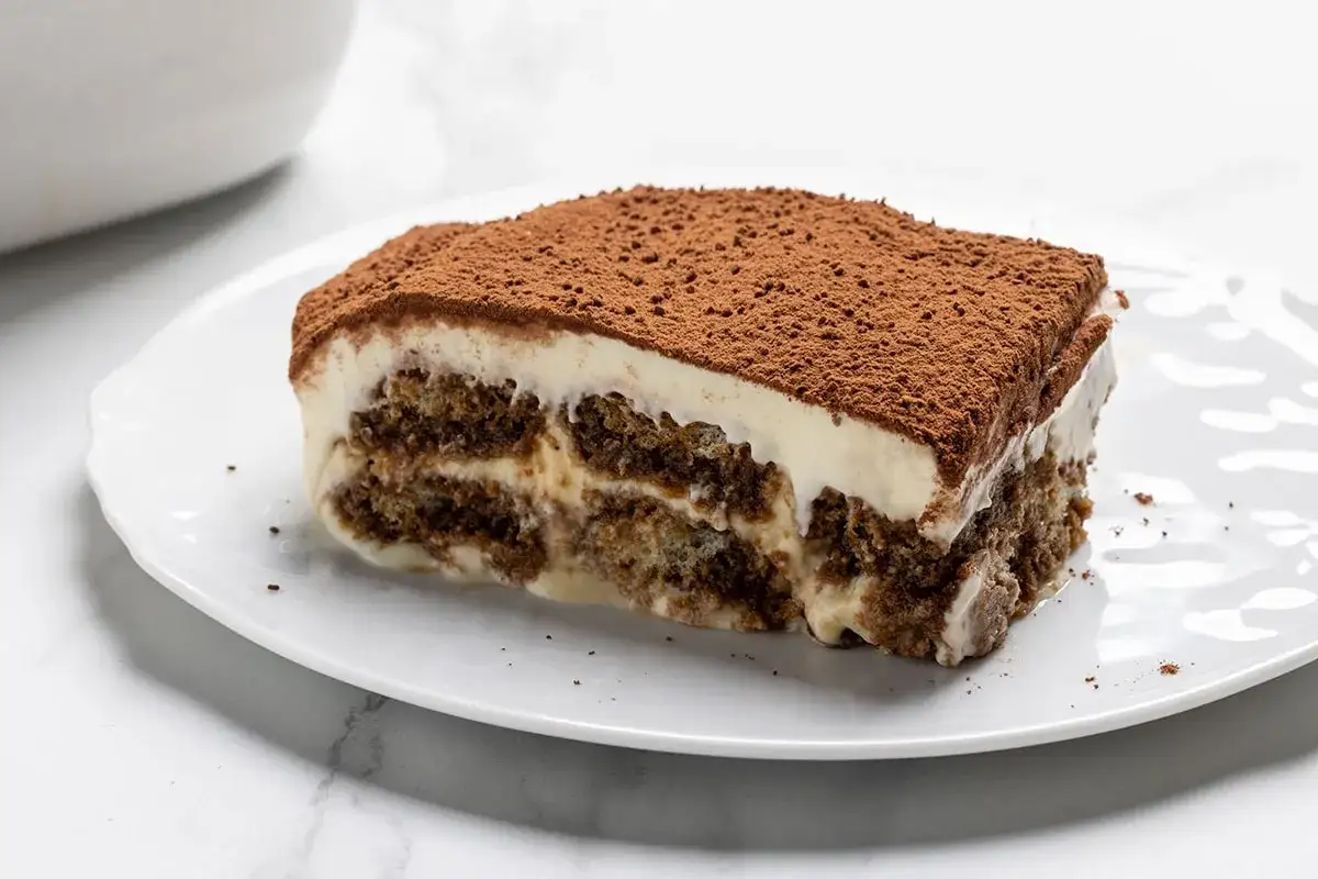 Una fetta di tiramisù fatto in casa, con strati di savoiardi inzuppati e crema al mascarpone, spolverata di cacao amaro.