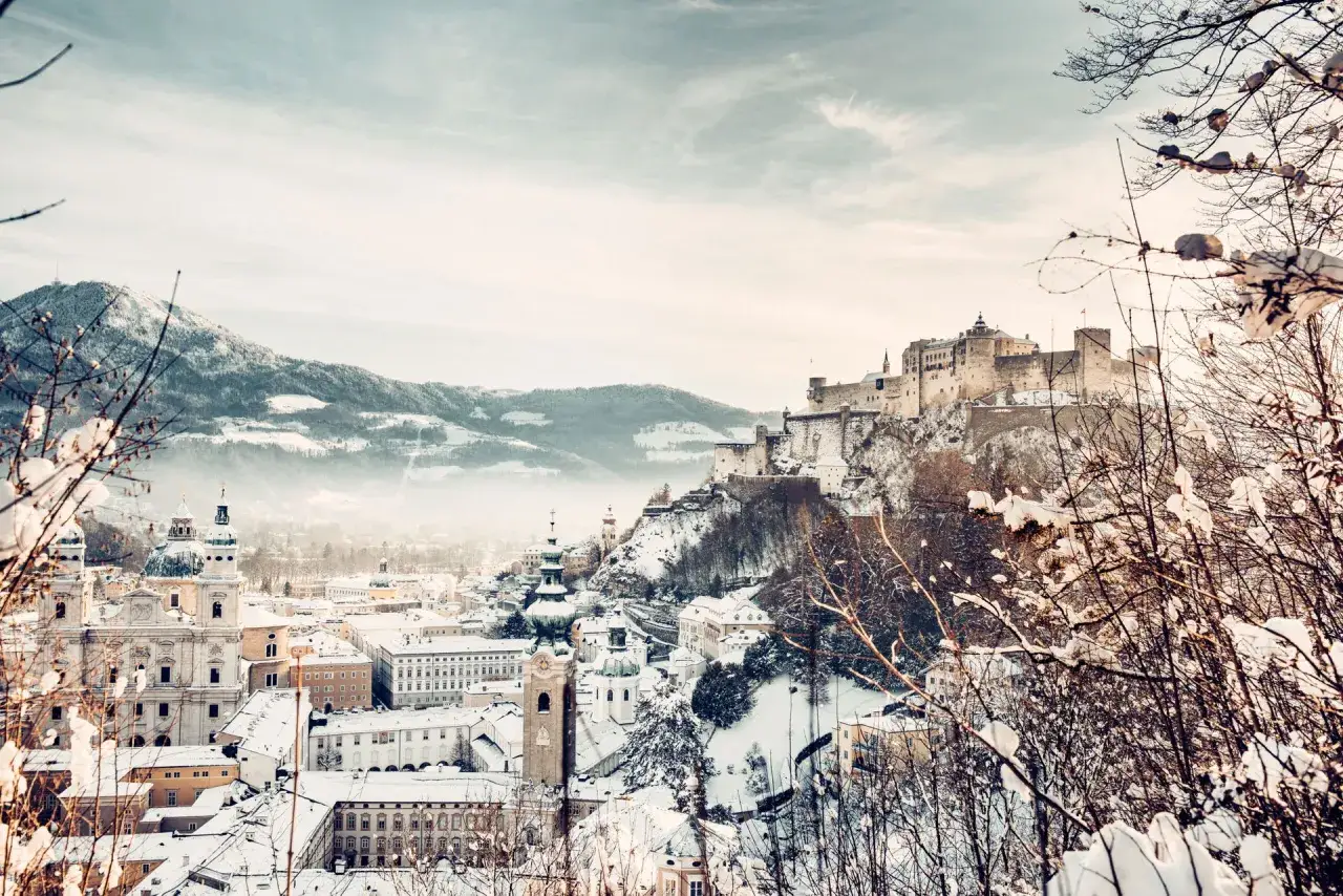 Salzburg im Winter: Festung Hohensalzburg thront &uuml;ber schneebedeckter Stadt und Bergen.