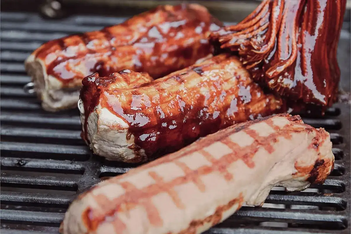 Mariniertes Fleisch grillen: Saftige Rippchen und eine Wurst brutzeln auf dem Rost. Der Duft von gegrilltem Fleisch liegt in der Luft.