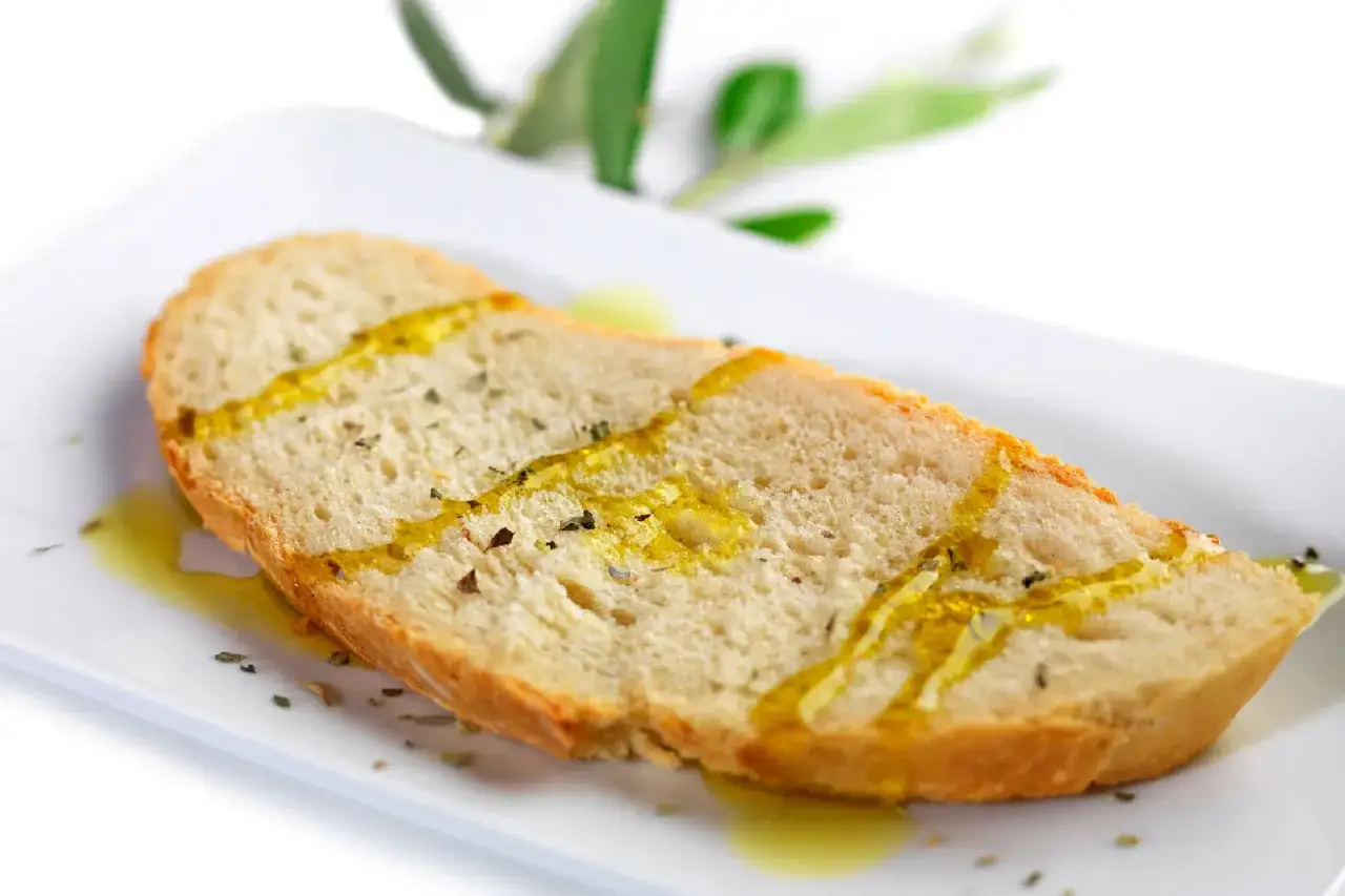 Bruschetta con olio d'oliva e erbe aromatiche su piatto bianco, con rametto di ulivo sullo sfondo.