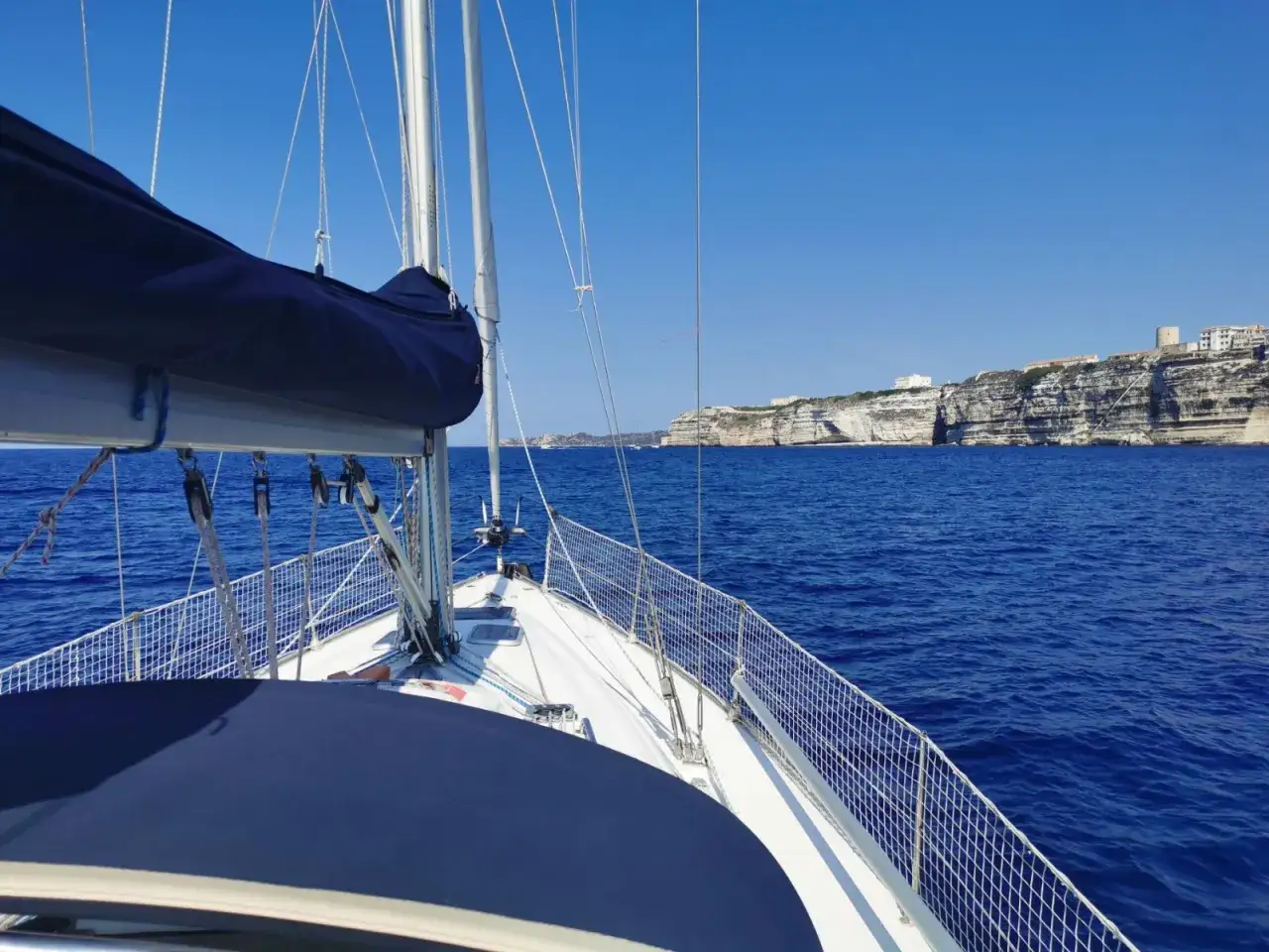 Vue depuis un voilier Bavaria 36, naviguant près de falaises blanches spectaculaires sous un ciel bleu.