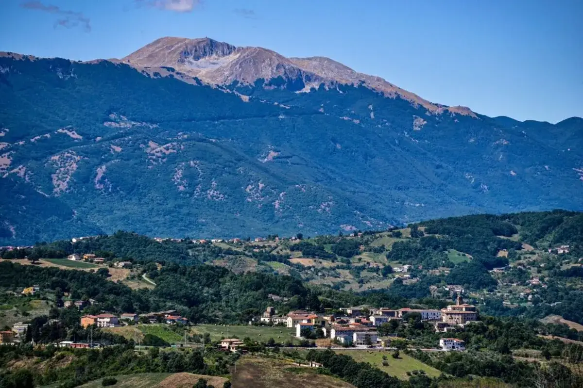 Piccoli paesi del Molise incastonati tra colline verdi e montagne imponenti, sotto un cielo azzurro.