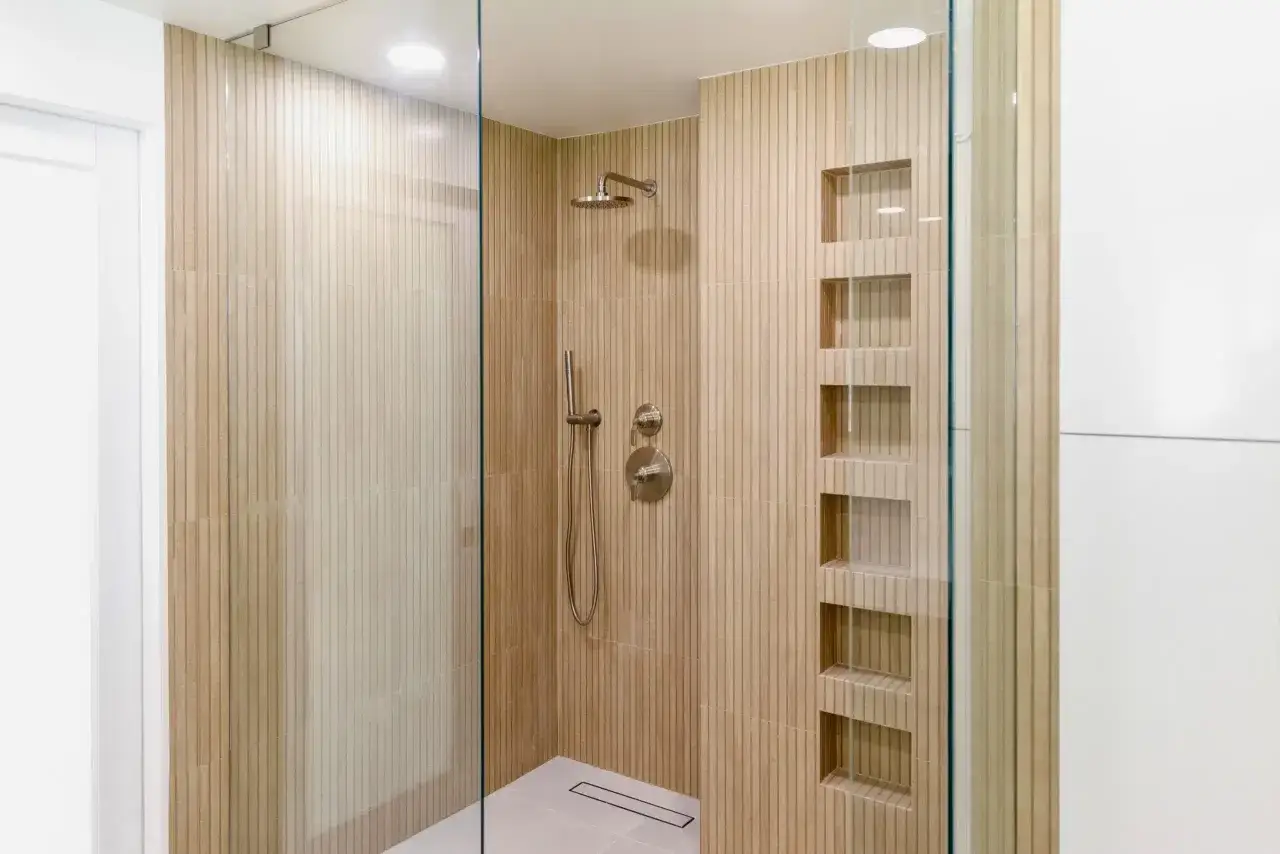 Douche moderne dans une salle de bain japandi, avec carrelage textur&eacute; en bois clair, niches int&eacute;gr&eacute;es et paroi en verre.