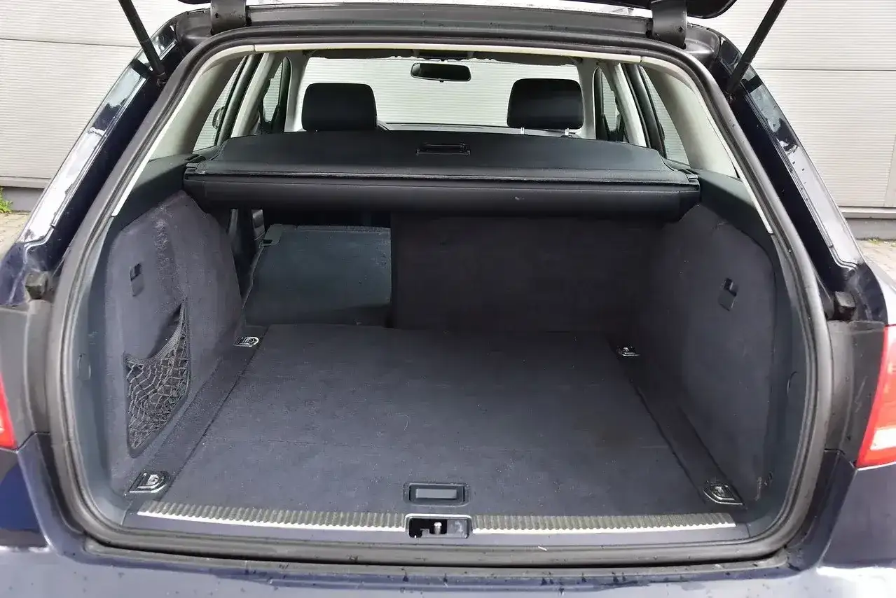 Audi A4 Avant 2.0 TDI z otwartym bagażnikiem. Wnętrze jest czyste, z siatką po lewej stronie i roletą bagażnika.
