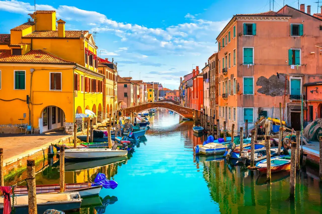 Colorate case affacciate su un canale con barche ormeggiate. Un ponte ad arco collega le sponde. Un'ottima idea per cosa fare a Chioggia, godersi la vista e l'atmosfera.