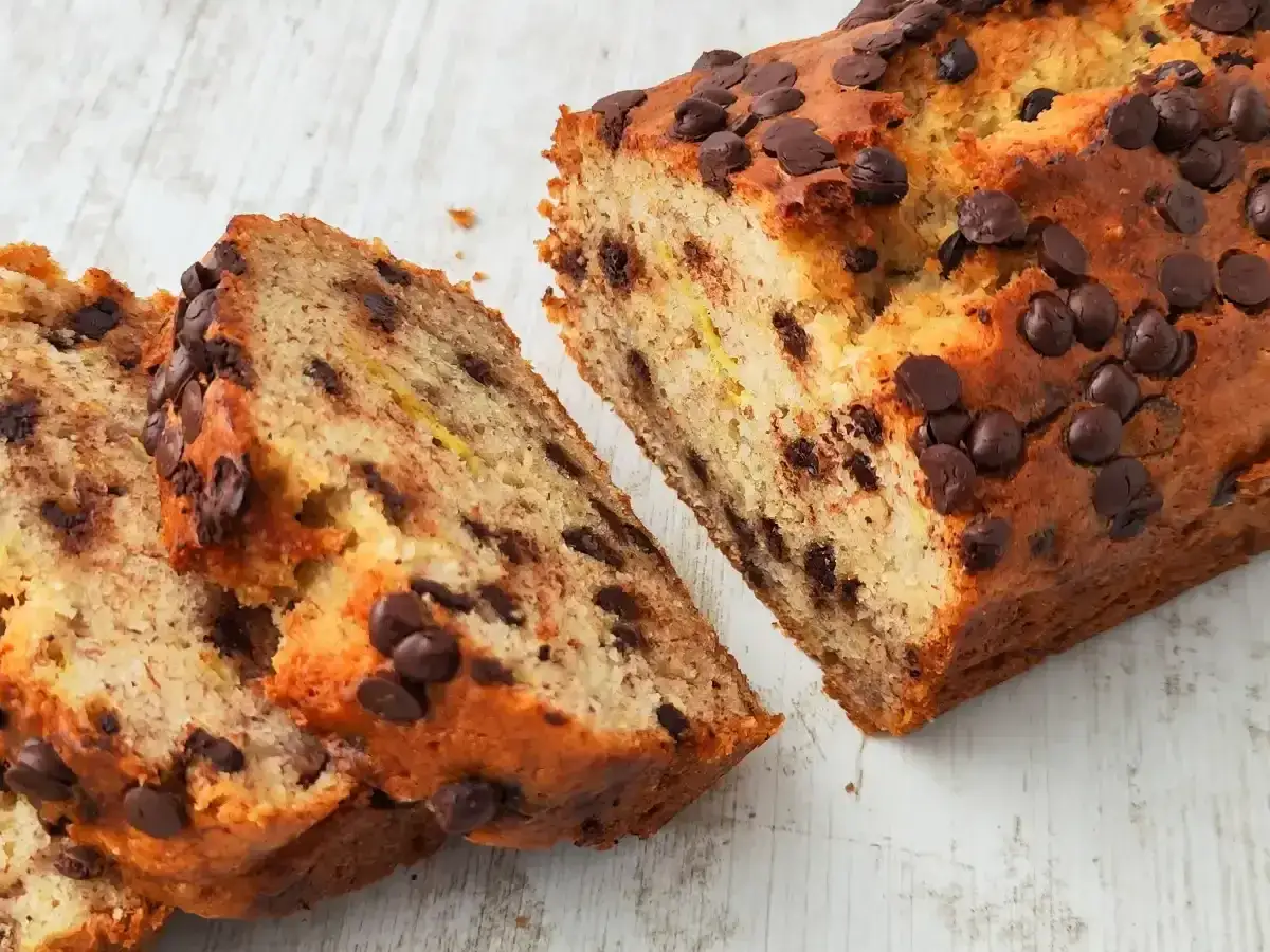 Saftiges, veganes Bananenbrot mit vielen Schokost&uuml;ckchen, auf einem hellen Holztisch.