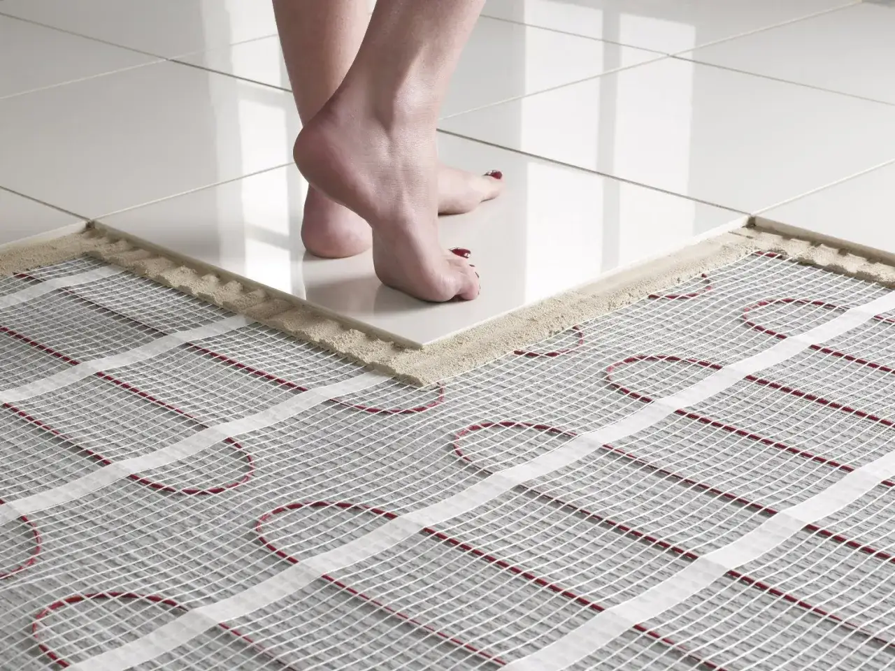 Piedi nudi su piastrelle lucide, con una parte del pavimento che mostra la rete per il riscaldamento a pavimento in bagno.