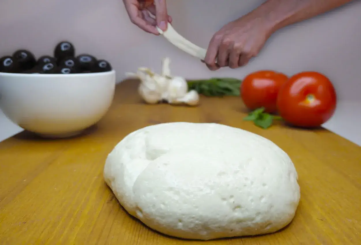 Masa para pizza con ingredientes frescos: tomates, aceitunas, ajo y mozzarella vegana estirándose.