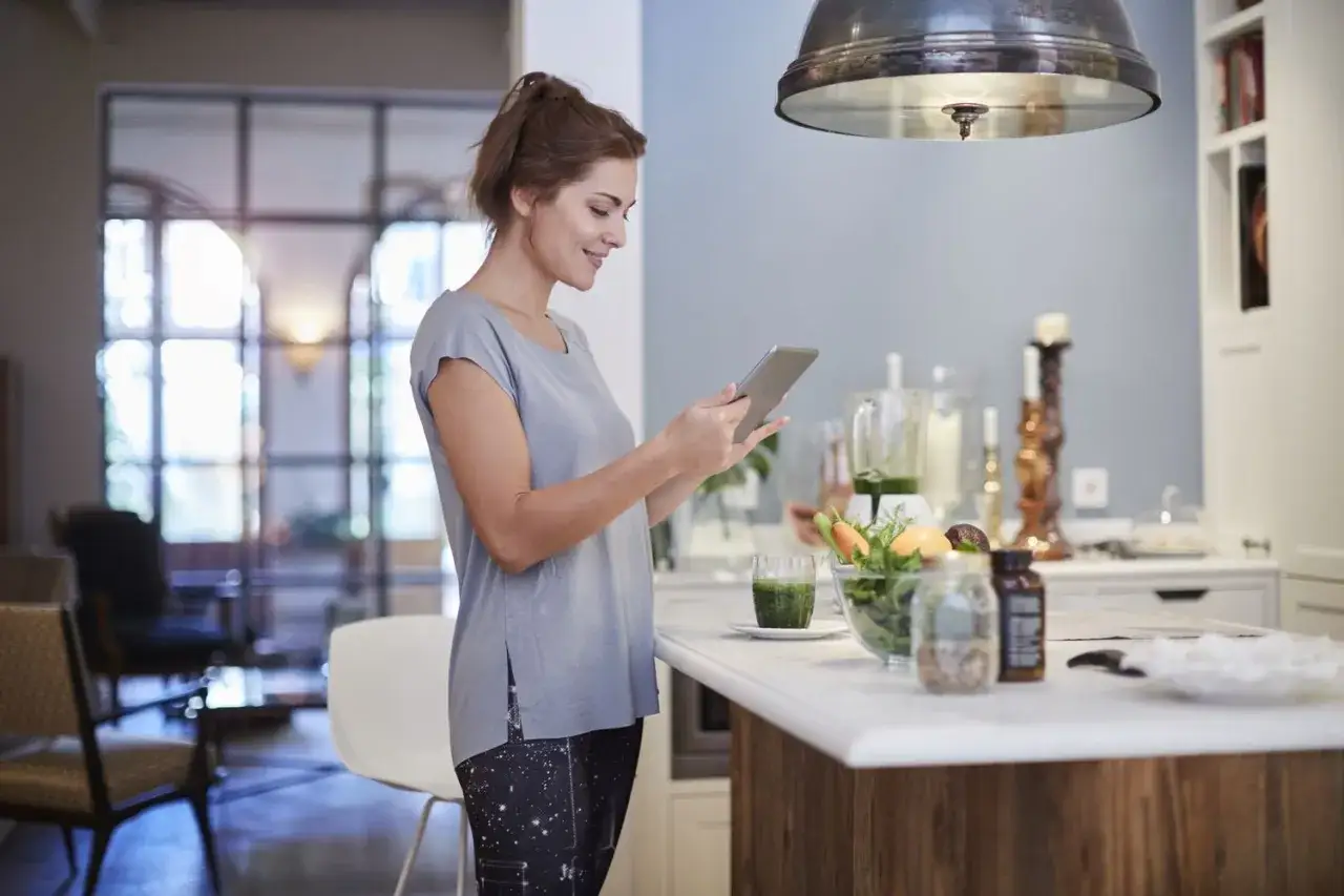 Kobieta z tabletem szuka inspiracji, jak zmotywować się do ćwiczeń. Na blacie stoją zdrowe przekąski i smoothie.