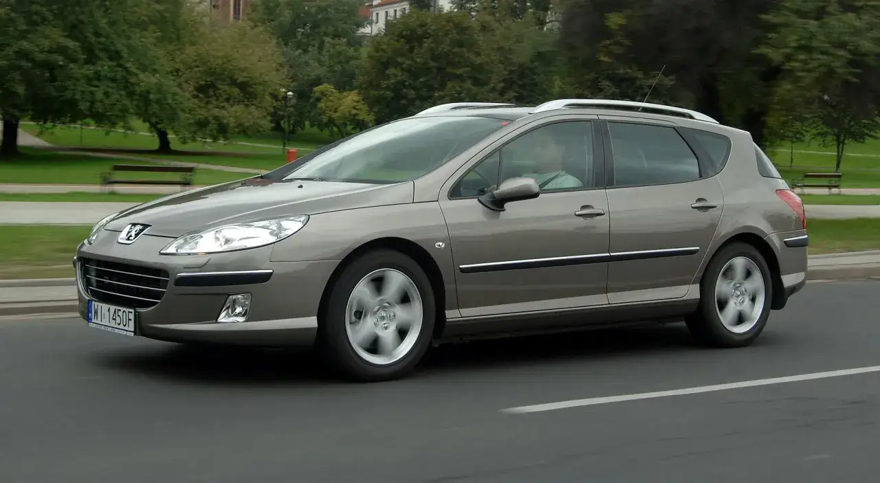 Szary Peugeot 407 SW w ruchu drogowym. Kierowca za kierownicą. Wiele osób chwali ten model, a opinie o Peugeot 407 są zazwyczaj pozytywne.