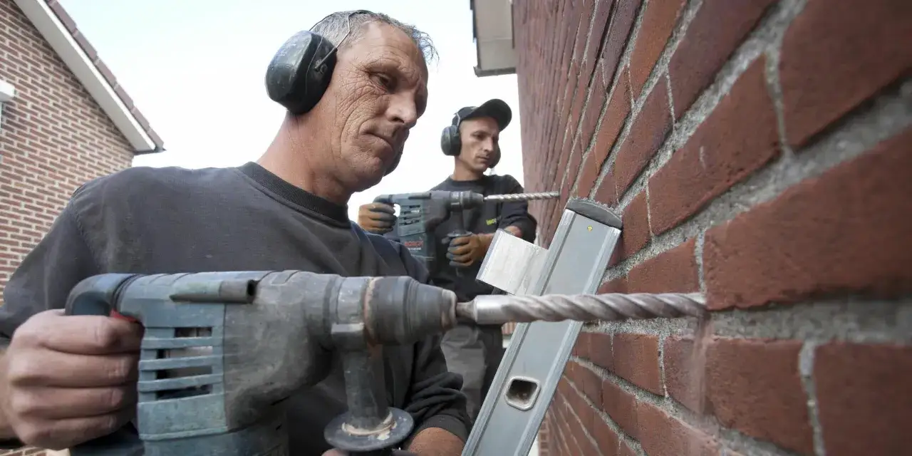 Deux ouvriers forent un mur de briques pour l'isolation par injection. Prix et devis pour une maison bien isolée.