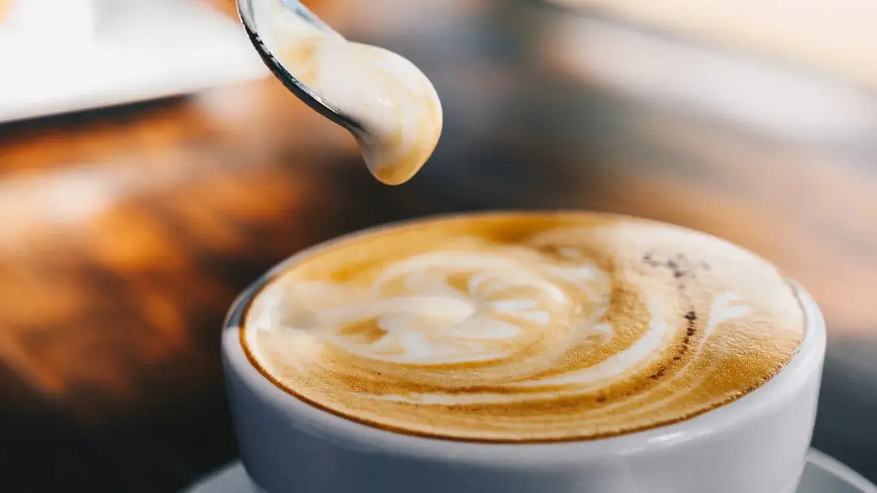 Ein Löffel mit Milchschaum über einem Cappuccino. Der Barista zeigt den perfekten Milchschaum, der den Unterschied macht.