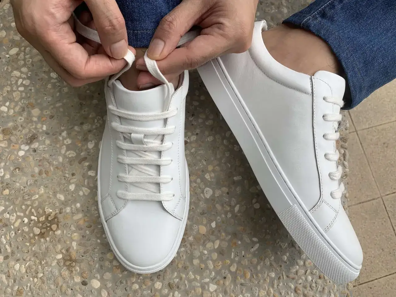 Mani che allacciano scarpe bianche, mostrando un modo per allacciare le scarpe senza far vedere i lacci, per un look pulito.