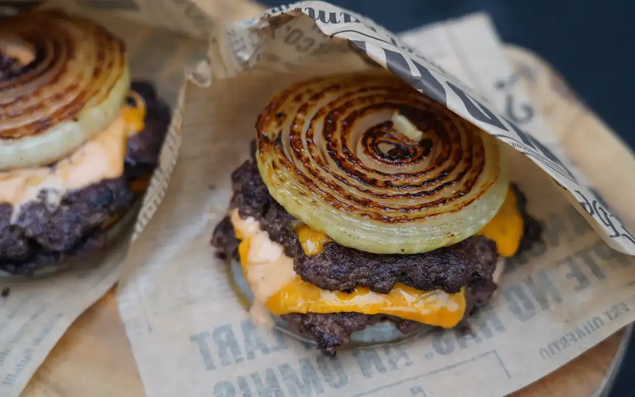 Ein saftiger Flying Dutchman Burger mit geschmolzenem K&auml;se und karamellisierten Zwiebelringen, eingewickelt in Papier.