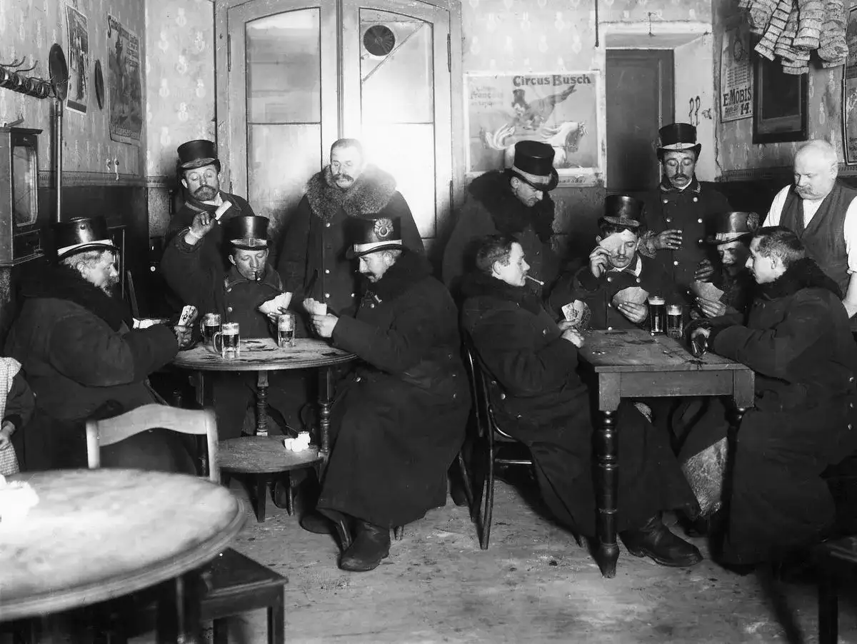 Männer in Zylindern und Mänteln spielen Karten in einer Kneipe. Ein Einblick in die **Gesellschaft im Kaiserreich**, wo Bier und Kartenspiele zur Unterhaltung gehörten.