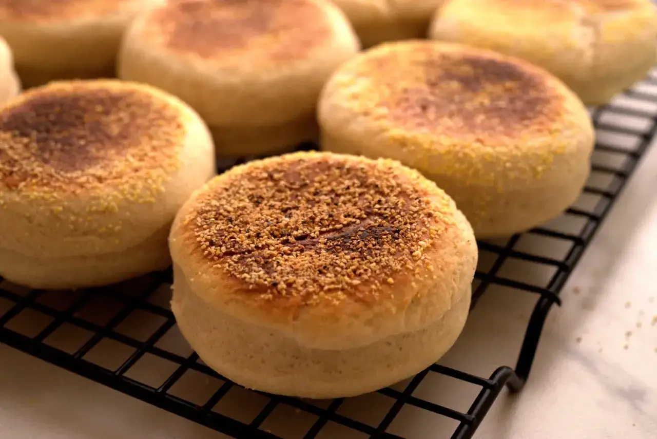 Plusieurs muffins anglais dor&eacute;s, parsem&eacute;s de semoule de ma&iuml;s, refroidissent sur une grille.