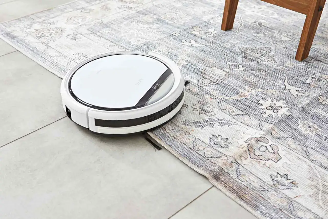 En vit robotdammsugare navigerar över en mönstrad matta, redo att ta sig an dammet.