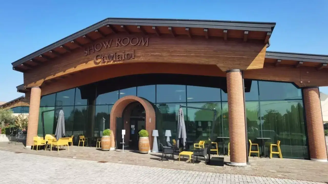 Show Room Ca Maiol a Sirmione, con ampie vetrate e arredi esterni colorati.
