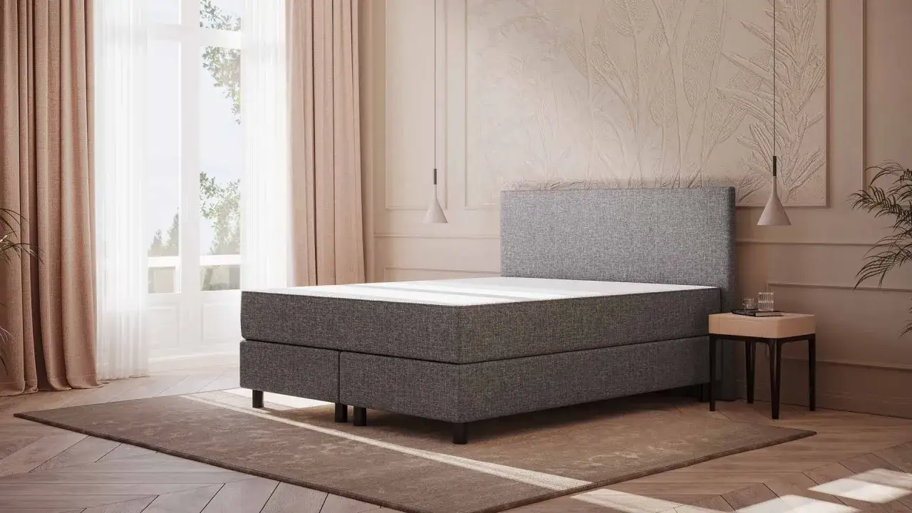 Ein modernes Bett mit grauem Stoffbezug und einer weißen Matratze. Vielleicht ist die Emma Matratze zu hart für einen erholsamen Schlaf.
