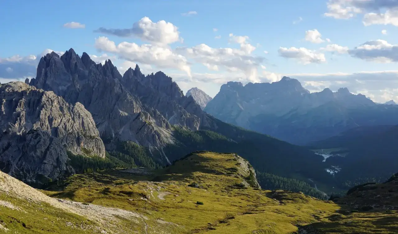 Majestatyczne szczyty Cadini di Misurina w Dolomitach, oświetlone słońcem, z zielonymi zboczami i błękitnym niebem.