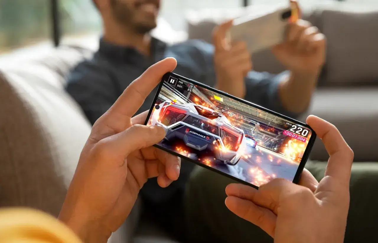 Dw&oacute;ch mężczyzn gra w wyścigowe gry na telefonie. Na ekranie widać pędzący samoch&oacute;d w grze Asphalt 5.
