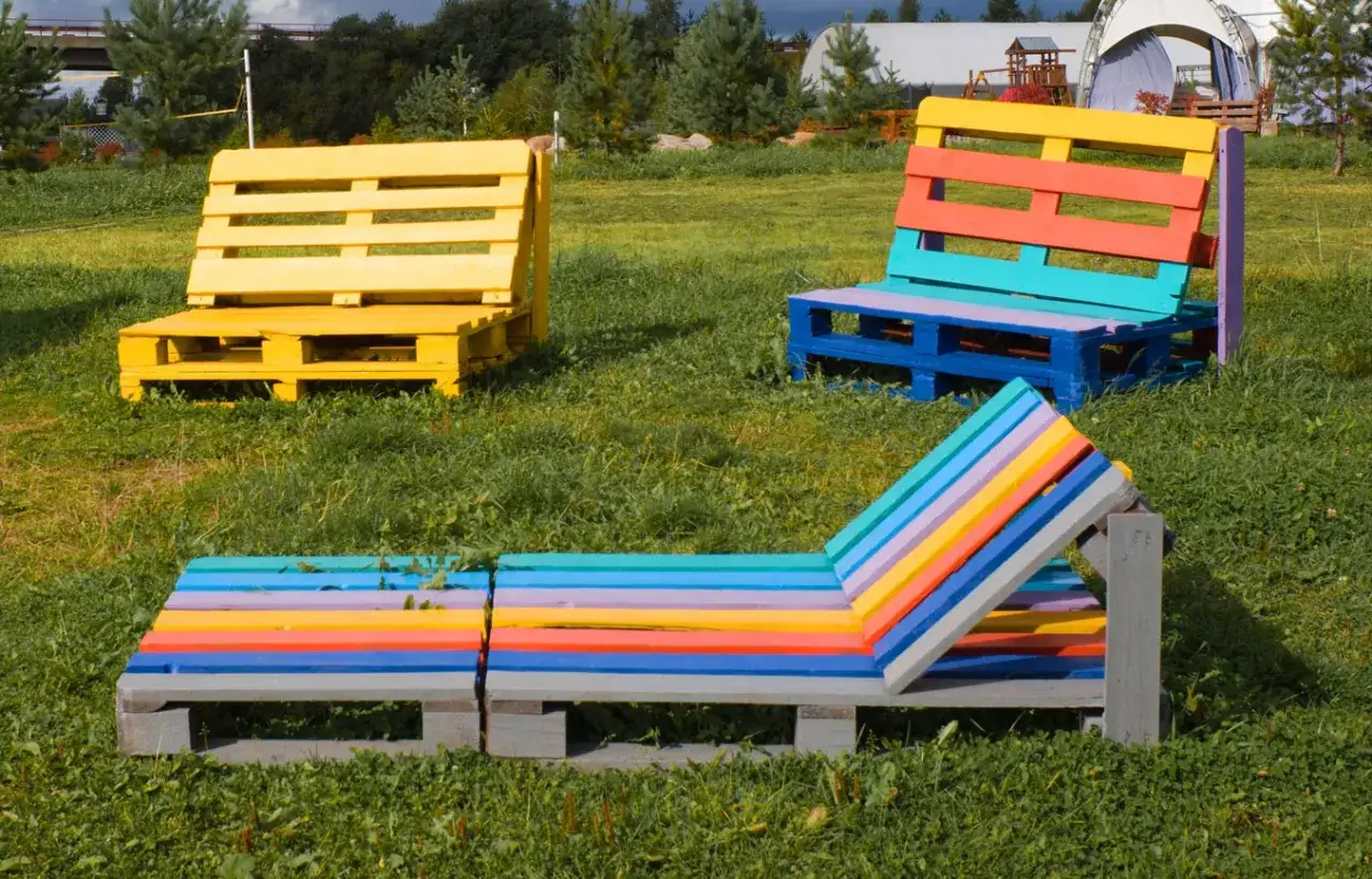 Bunte Palettenmöbel im Garten: Eine Liege und zwei Bänke, farbenfroh gestaltet. Paletten streichen ohne schleifen ist hier die Devise für kreative Deko.