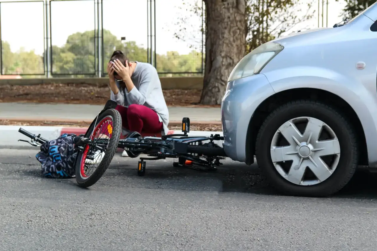 Vrouw met handen voor gezicht na fietsongeval met auto. Fiets ligt op straat. Mogelijk recht op schadevergoeding fietsongeval.