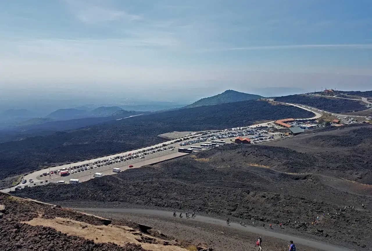 Parcheggio affollato per chi decide di visitare l'Etna con la propria auto. Paesaggio lunare di lava nera.