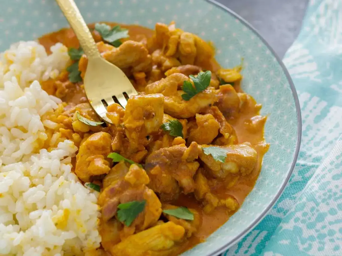 Un delicioso pollo al curry, con su arroz blanco y un tenedor dorado, listo para disfrutar. &iquest;De donde es el pollo al curry? &iexcl;De la India, por supuesto!