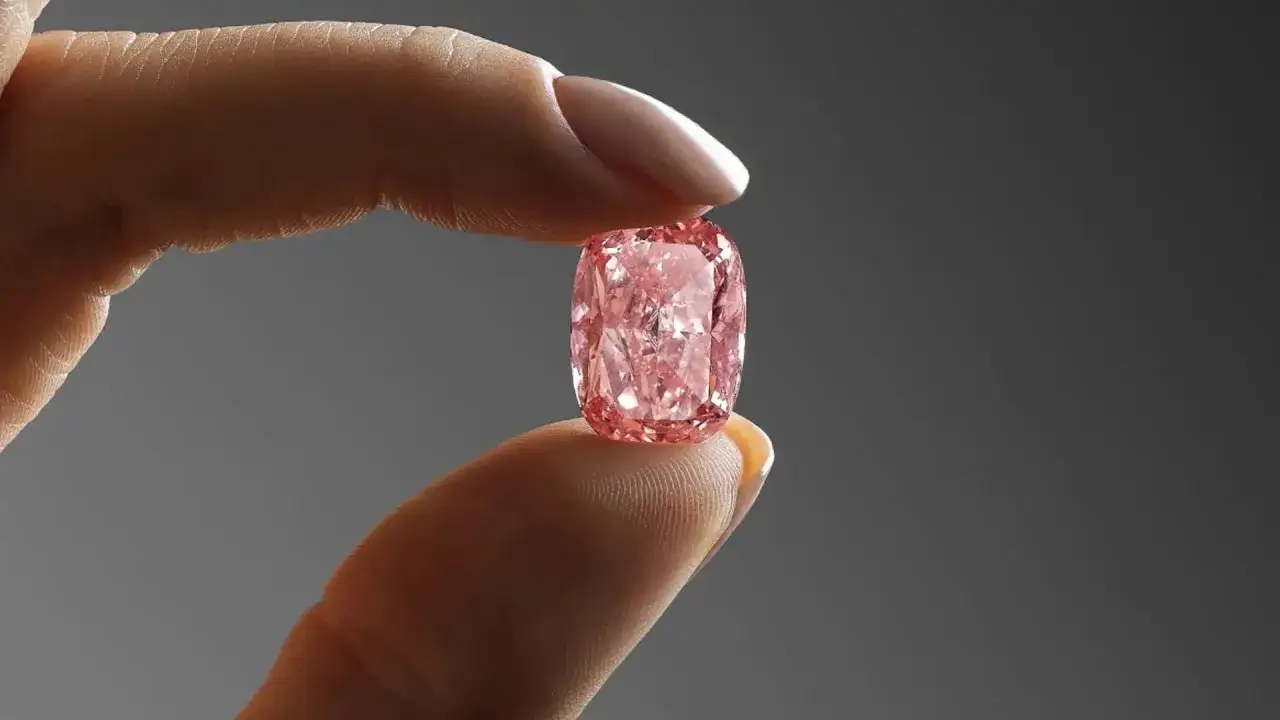 Ein Finger hält einen leuchtend pinken Diamanten, der wie der teuerste Diamant der Welt aussieht. Sein Preis ist unvorstellbar.