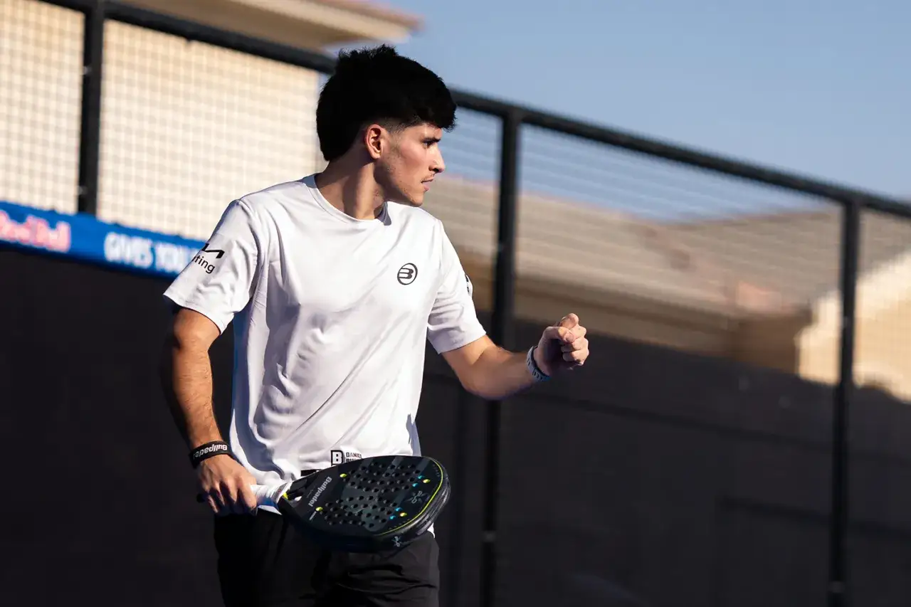 Maxi Sanchez, giocatore di padel, esulta con il pugno chiuso e la racchetta in mano, pronto per il prossimo punto.