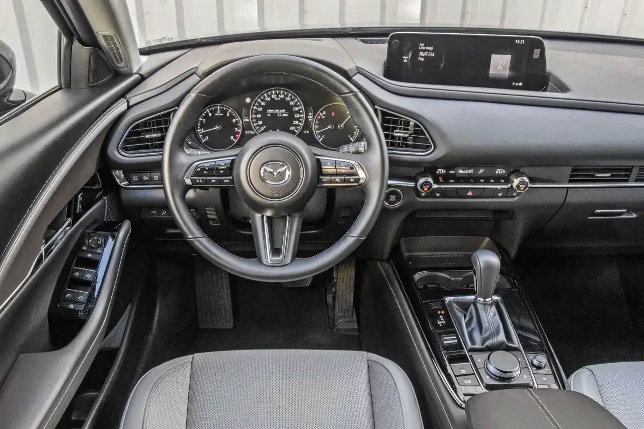 Wnętrze Mazdy CX-30: kierownica, deska rozdzielcza z ekranem multimediów i panelem klimatyzacji. Sprawdź mazda cx 30 cena.