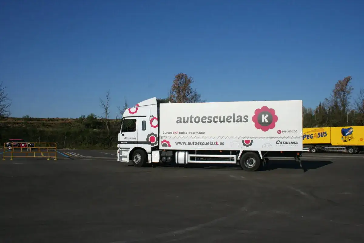 Camión de autoescuelas con remolque blanco y flores rojas. Averigua cuanto cuesta el carnet de trailer.